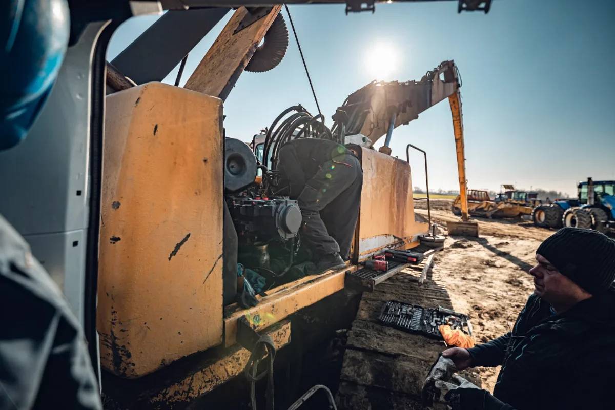 Monteur an der Hydraulikpumpe eines Baggers bei einer Reparatur auf der Baustelle