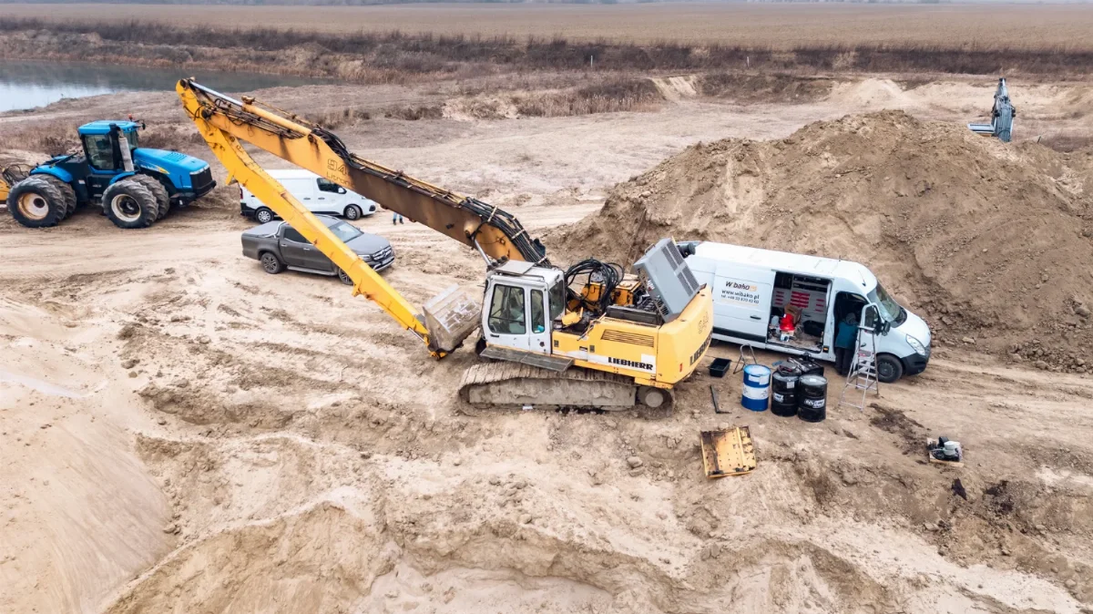 Liebherr Kettenbagger mit Long-Front-Ausrüstung bei der Wartung in einer Kiesgrube neben dem WIBAKO Servicewagen und Ölfässern