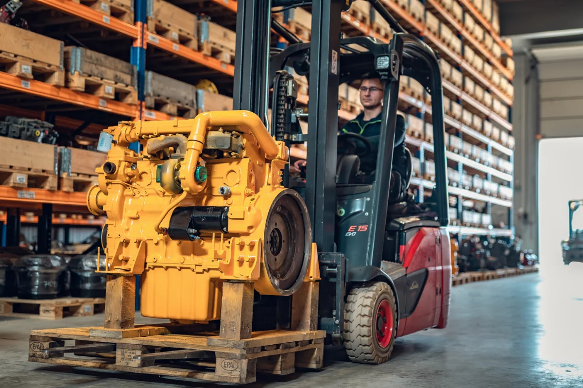 Gabelstapler transportiert einen überholten gelben Dieselmotor auf einer Palette in der Lagerhalle