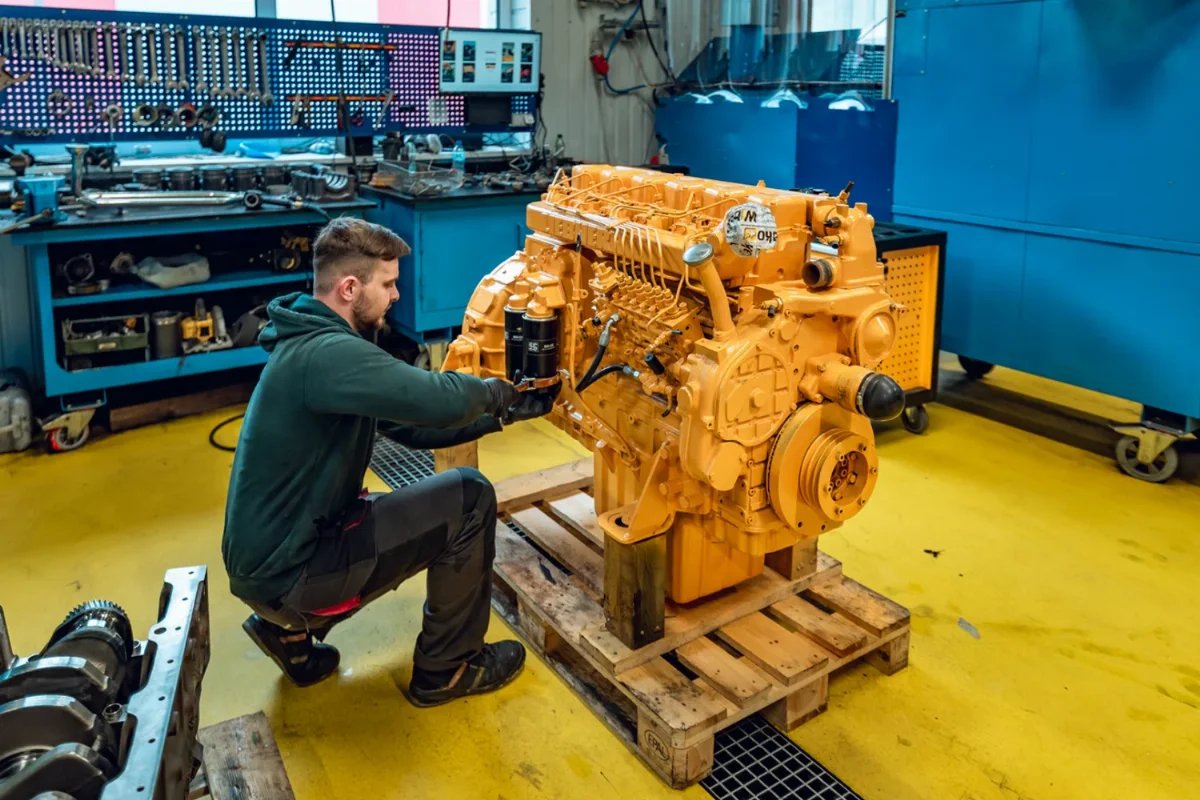 Mechaniker montiert Filter an einem überholten, gelb lackierten Dieselmotor auf einer Palette