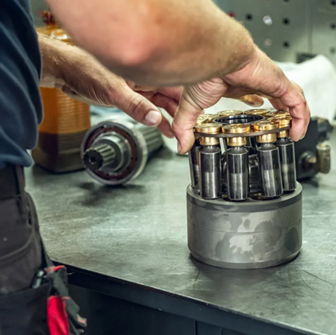 Mechaniker montiert eine Zylindertrommel mit Kolben auf der Werkbank, daneben Welle mit Lager