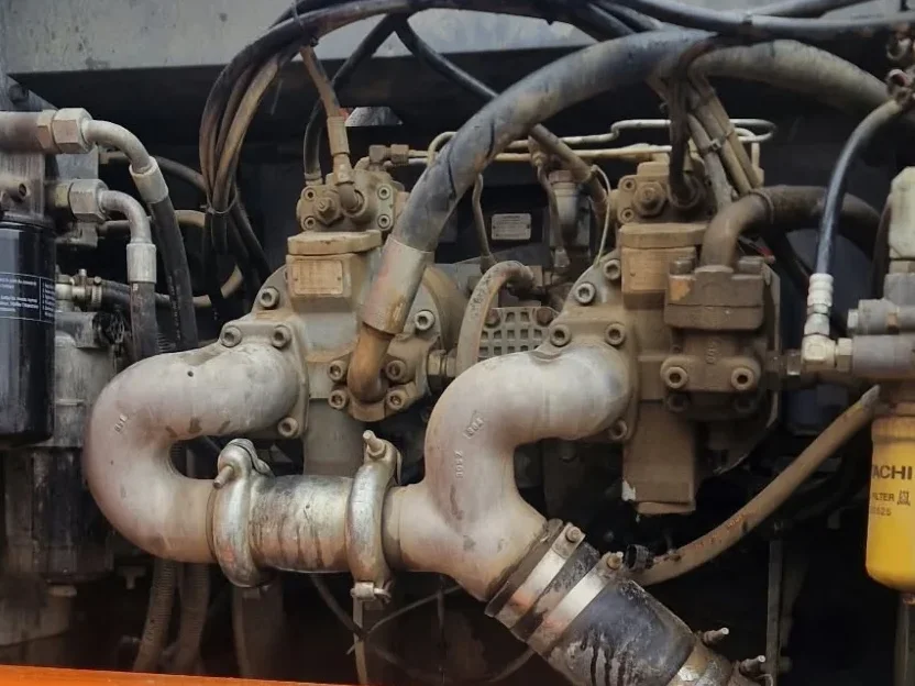 Pumpenraum eines Hitachi ZX350LC-3 mit Saugrohren der Hydraulikpumpe, darunter ein Fass für das abgelassene Öl