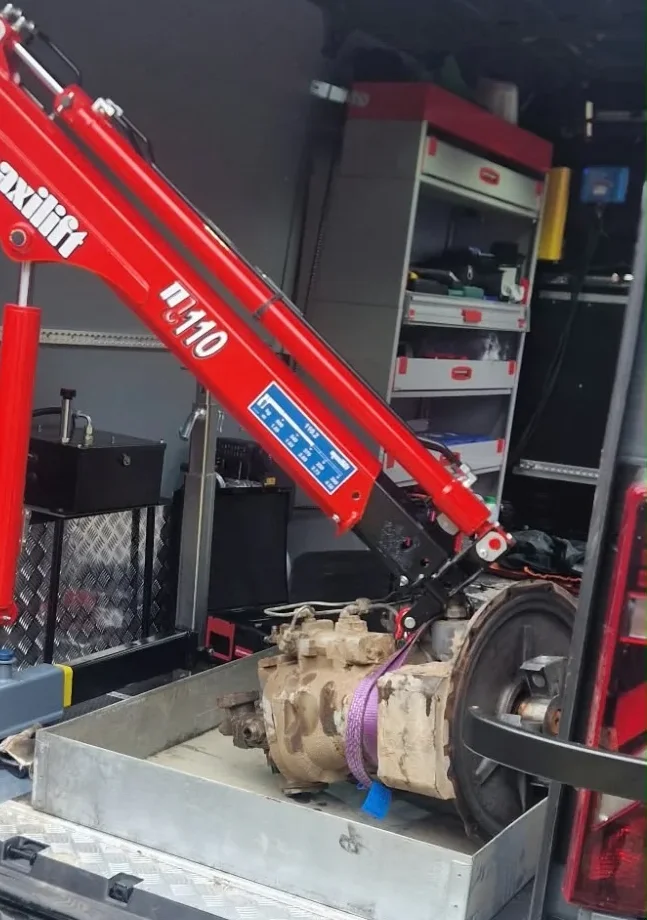 Ausgebaute Bagger-Hydraulikpumpe in einer Wanne im Servicewagen unter dem Arm eines roten Ladekrans